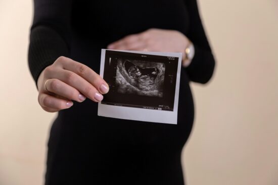 Cropped image of young pregnant woman holding ultrasound picture on belly.